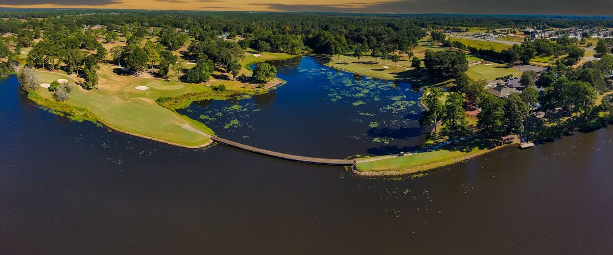 an aerial panoramic shot of a blue waters of Houston Lake surrounded by a golf course and lush green trees, grass and plants with powerful clouds at sunset in Perry Georgia USA
