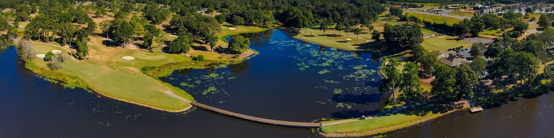 an aerial panoramic shot of a blue waters of Houston Lake surrounded by a golf course and lush green trees, grass and plants with powerful clouds at sunset in Perry Georgia USA