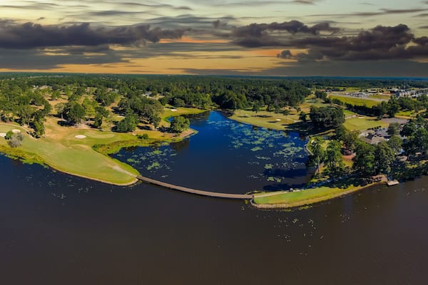 an aerial panoramic shot of a blue waters of Houston Lake surrounded by a golf course and lush green trees, grass and plants with powerful clouds at sunset in Perry Georgia USA