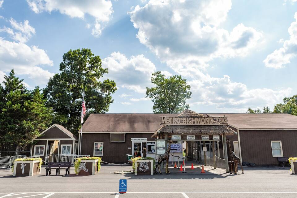 A zoo entrance with a giraffe statue, ticket booth, and a sign reading "Metro Richmond Zoo".