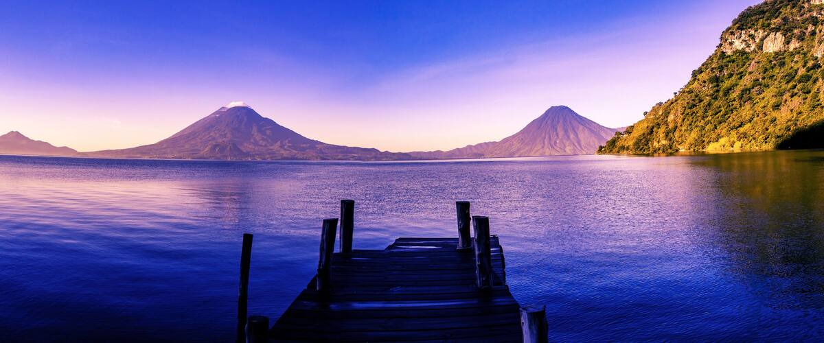 A wooden dock extending into calm waters with two prominent mountains in the background.