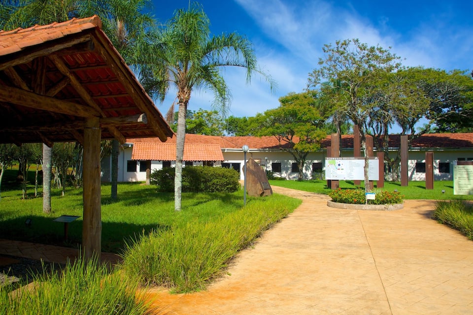 Uma trilha leva a um edifício com telhado de telhas vermelhas, cercado por vegetação e árvores.