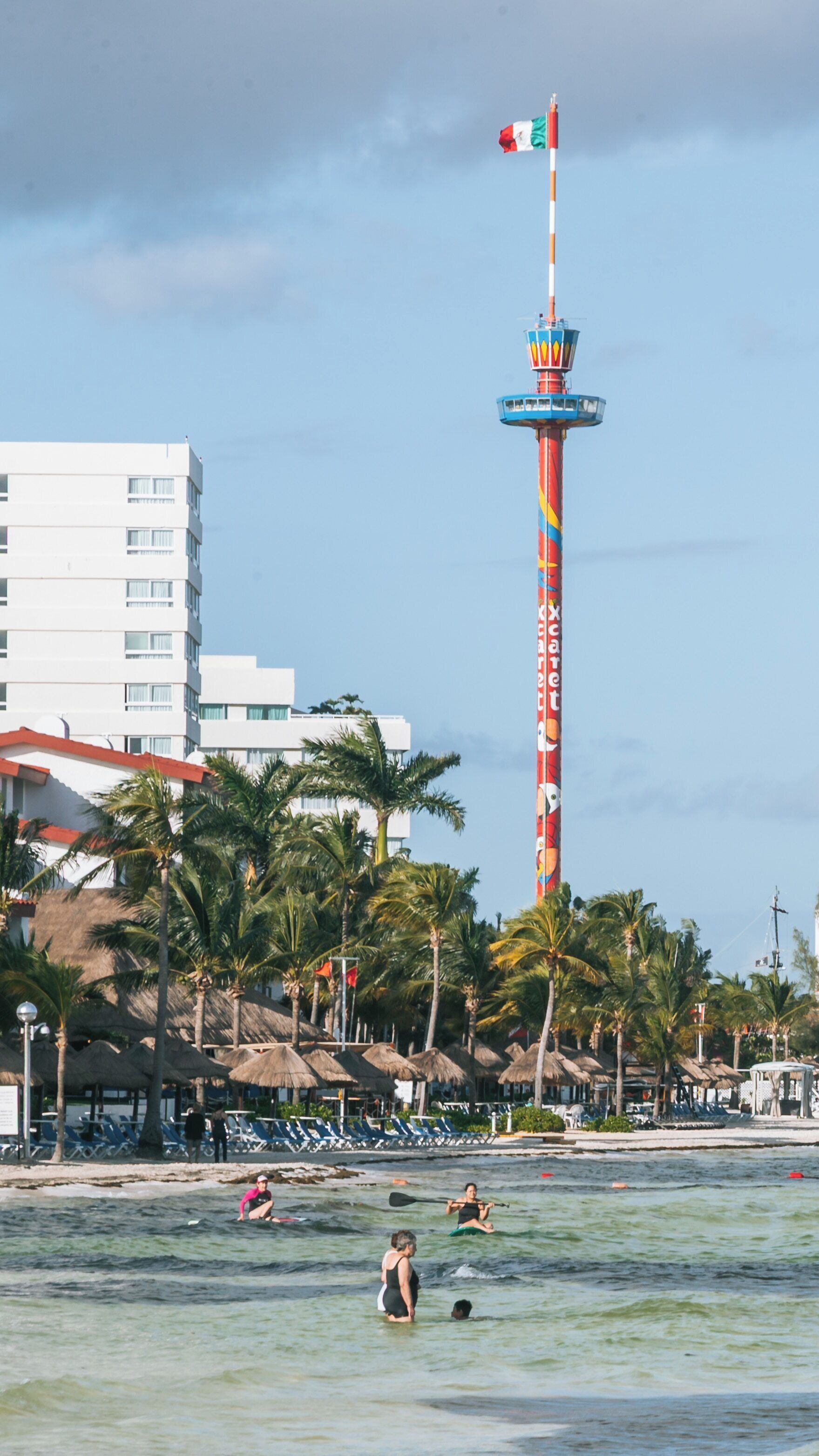 Vibrant Escenica Tower stands tall among palm trees and beachgoers in Cancun's Zona Hotelera during a sunny day