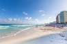Une plage avec une eau d’un bleu limpide, des gens qui prennent des bains de soleil et, au loin, un grand hôtel.