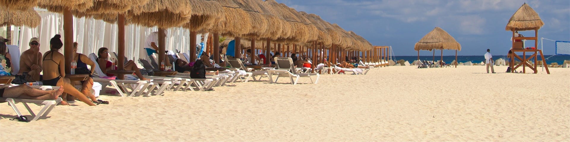 Une plage avec des parasols en chaume et des palmiers.