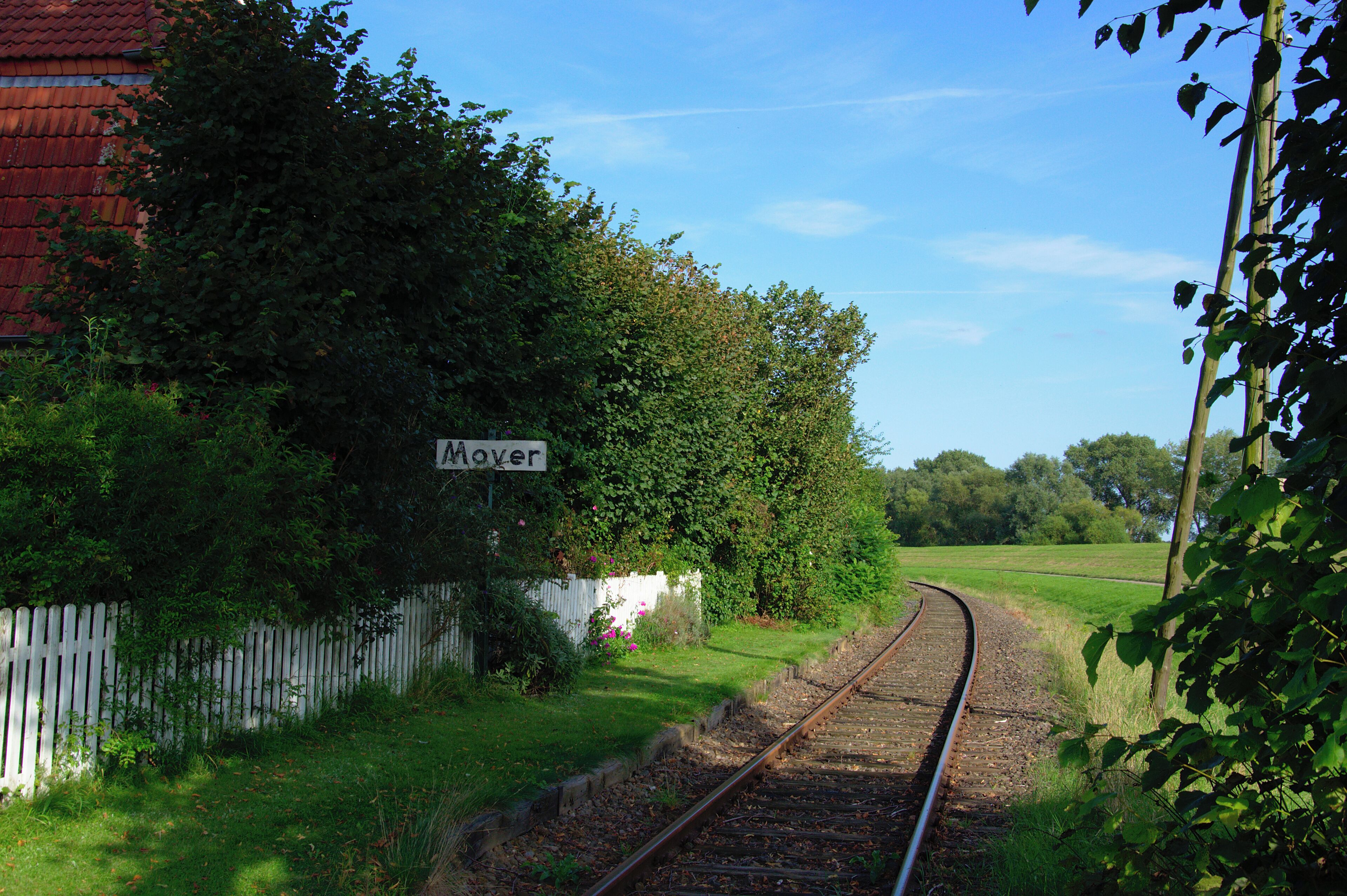 A railway track curving through a rural area with a sign reading "Moyer" and lush greenery.