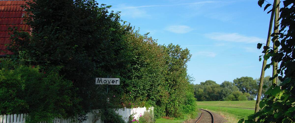 A railway track curving through a rural area with a sign reading "Moyer" and lush greenery.