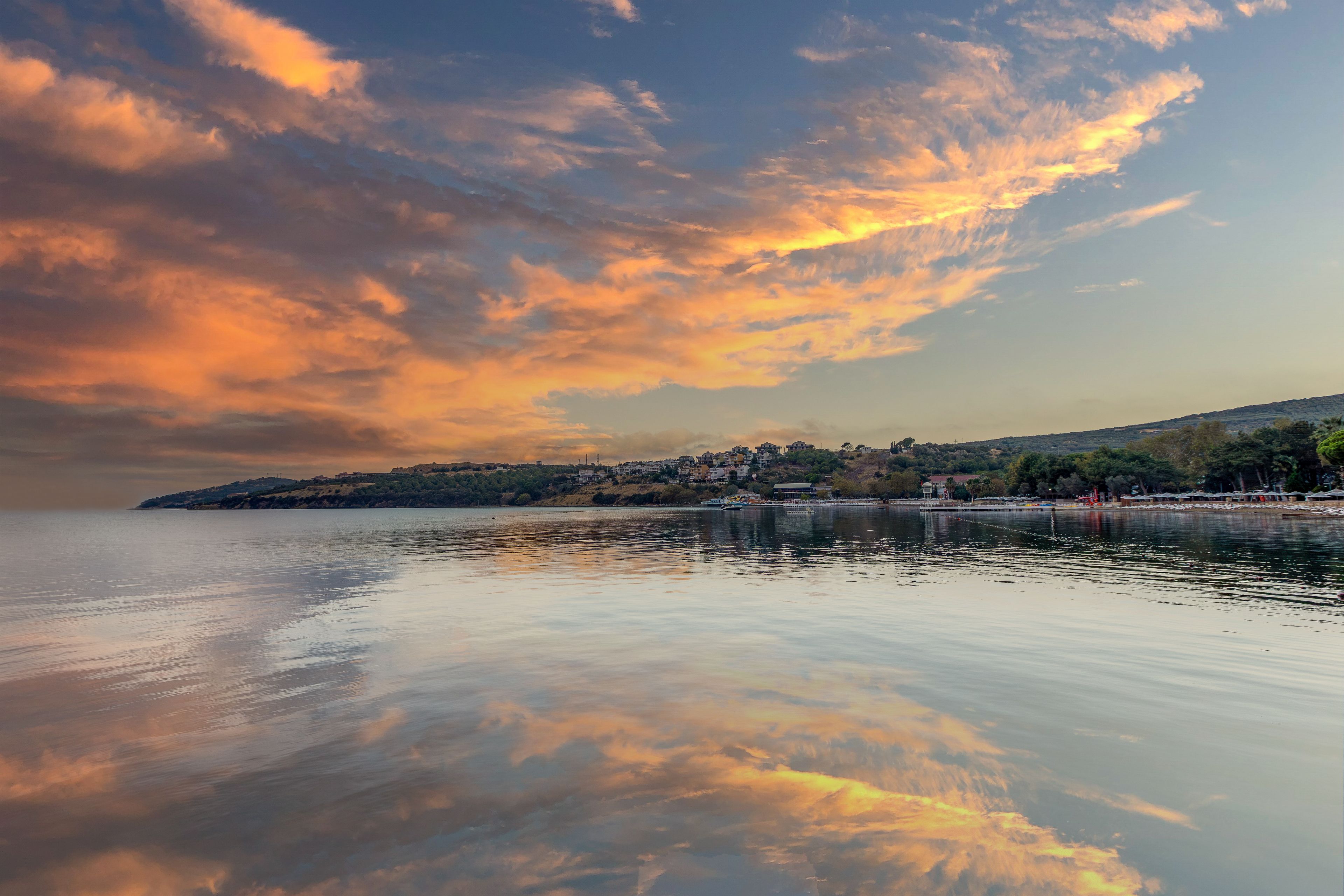 En rolig sø med en solnedgang reflekteret i vandet, en fjer shoreline og et bakket landskab.