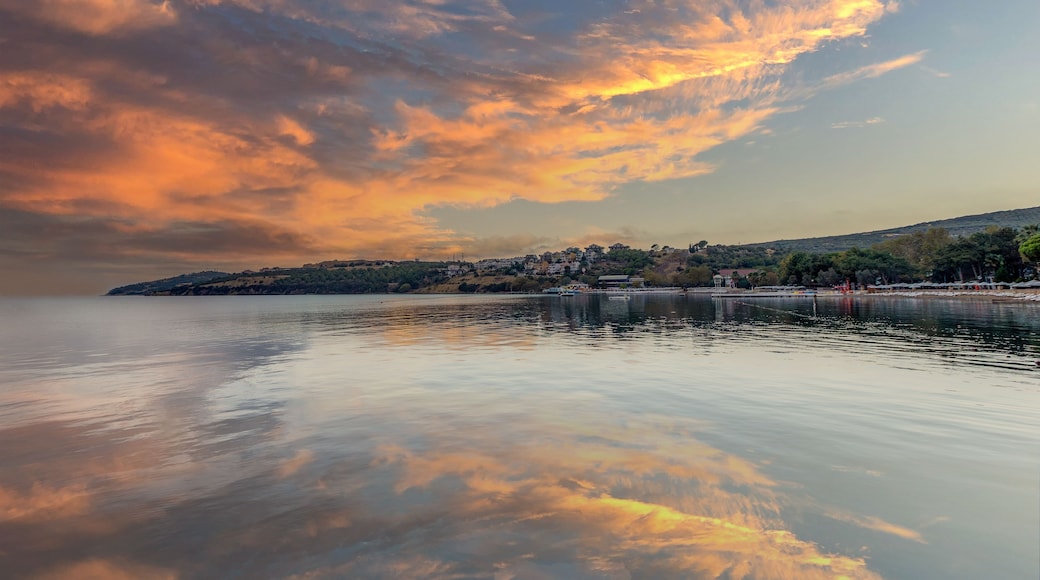 En rolig sø med en solnedgang reflekteret i vandet, en fjer shoreline og et bakket landskab.