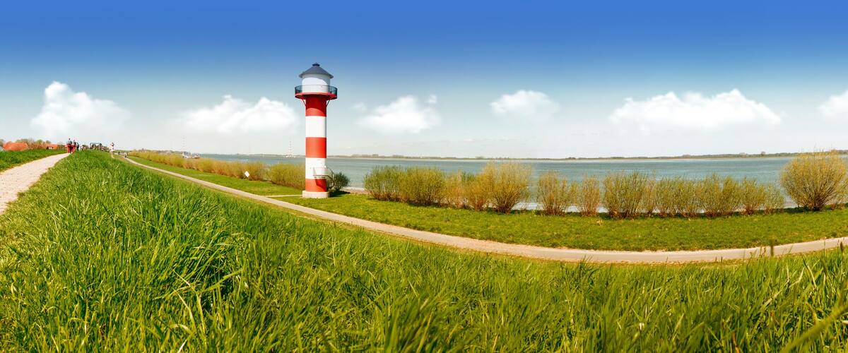 A red and white lighthouse, a grassy path, and a calm lake.