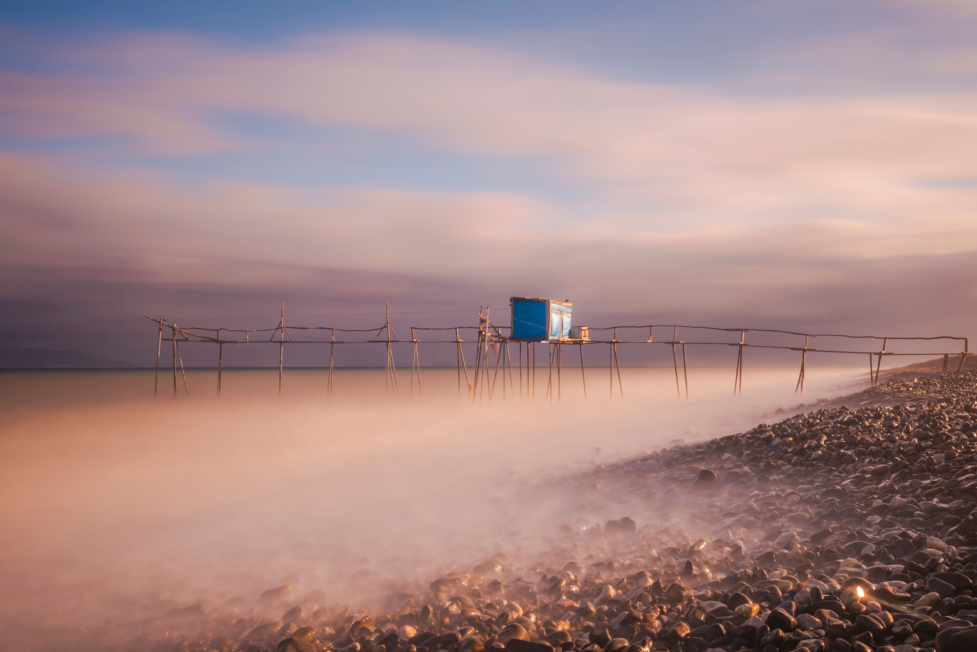 Ein Strand mit einer Holzlattenverkleidung und einer blauen Konstruktion auf Stelzen.