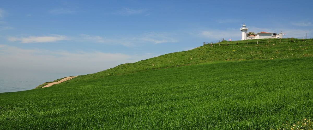 A lighthouse on a grassy hill with a clear blue sky.