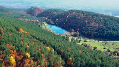 Paisagem montanhosa com um lago rodeado por árvores de tons outonais.