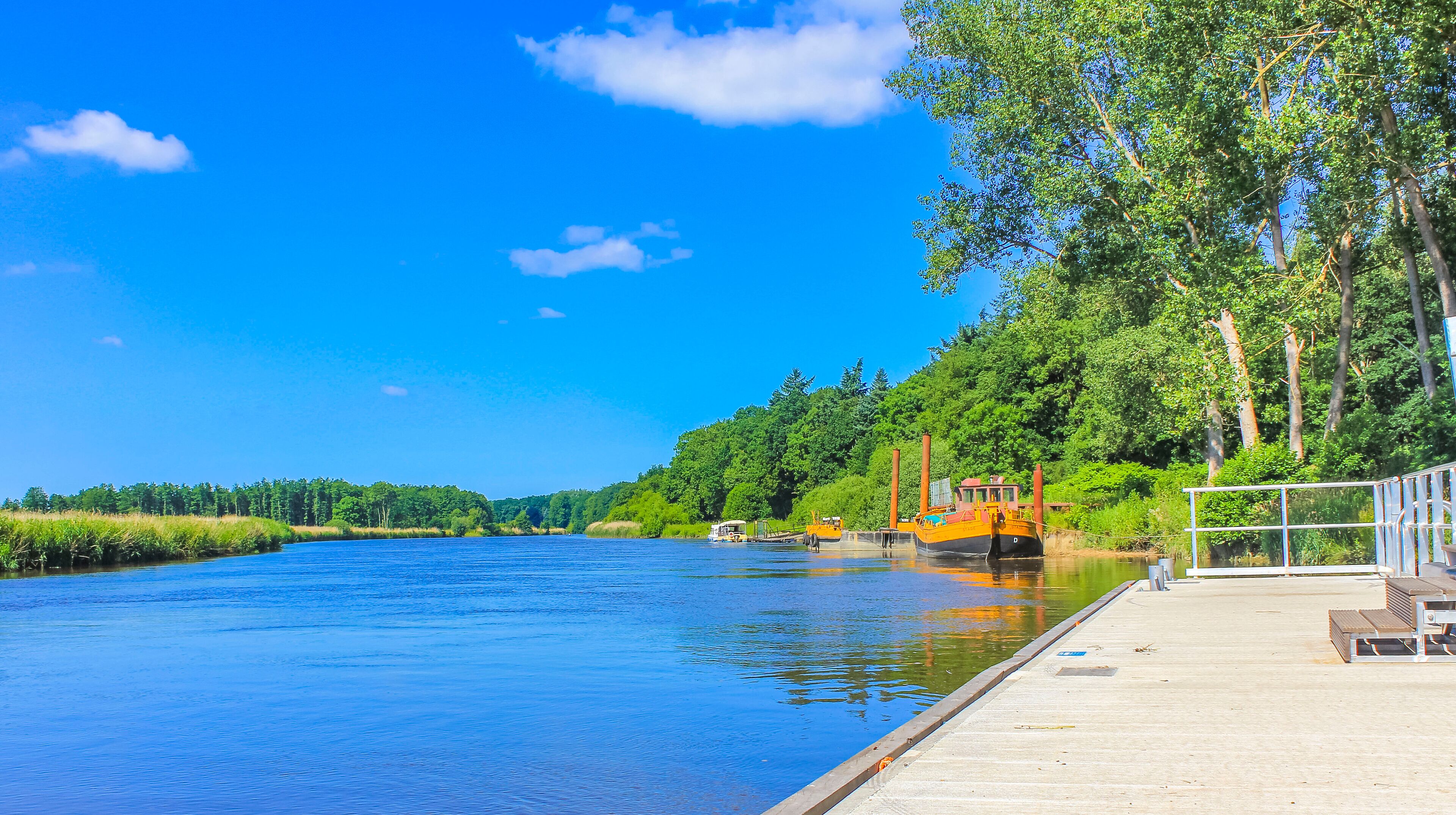 A river with a dock, boats, and a forested hillside.