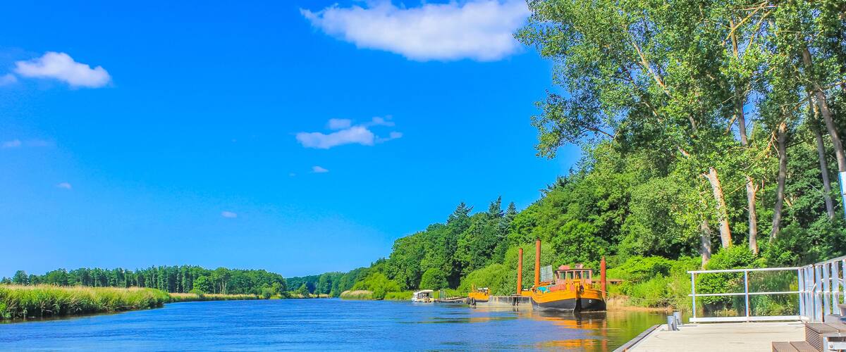 A river with a dock, boats, and a forested hillside.