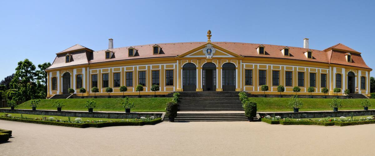 A large, yellow building with a symmetrical facade, arched windows, and a central entrance flanked by steps.