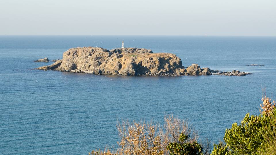 A rocky island with a lighthouse in the distance.