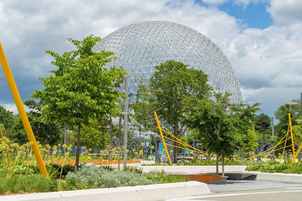 A large geodesic dome structure surrounded by trees and yellow poles.