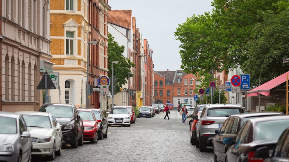 A cobblestone street lined with parked cars and historic buildings.