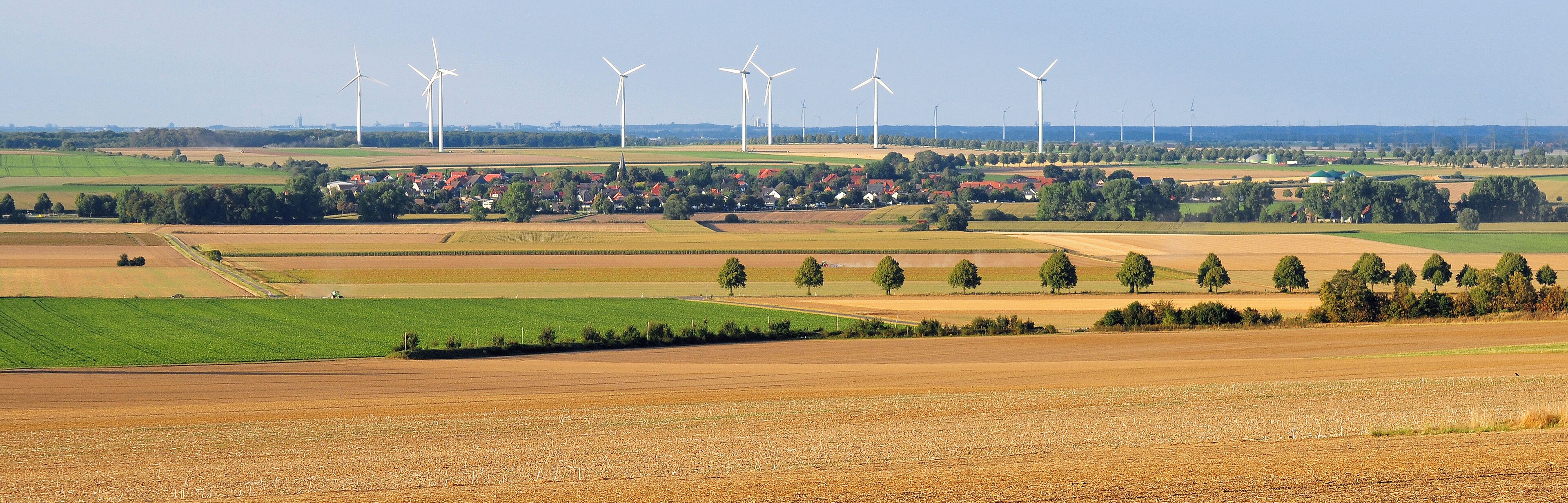 A rural landscape with wind turbines, fields, and a small village.