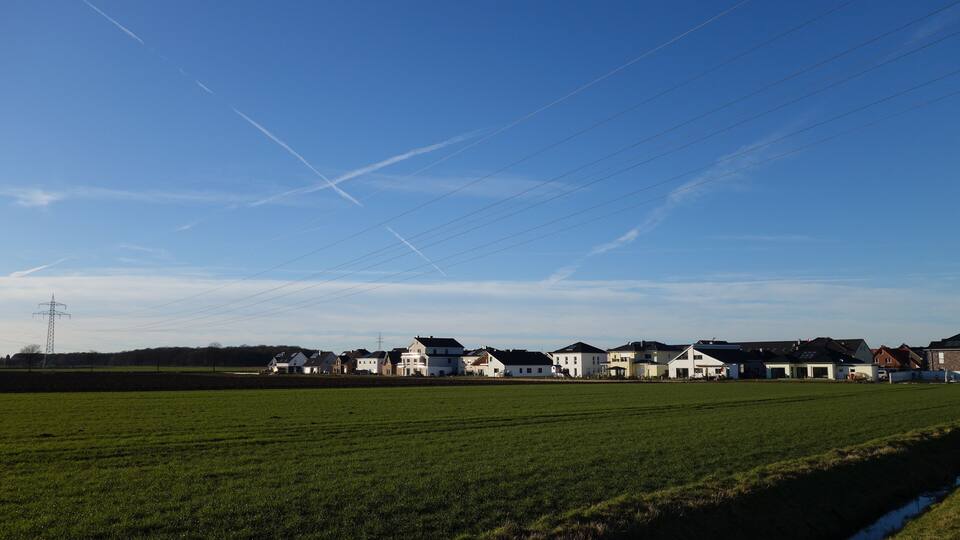 A rural landscape with a green field, a row of houses, and power lines.