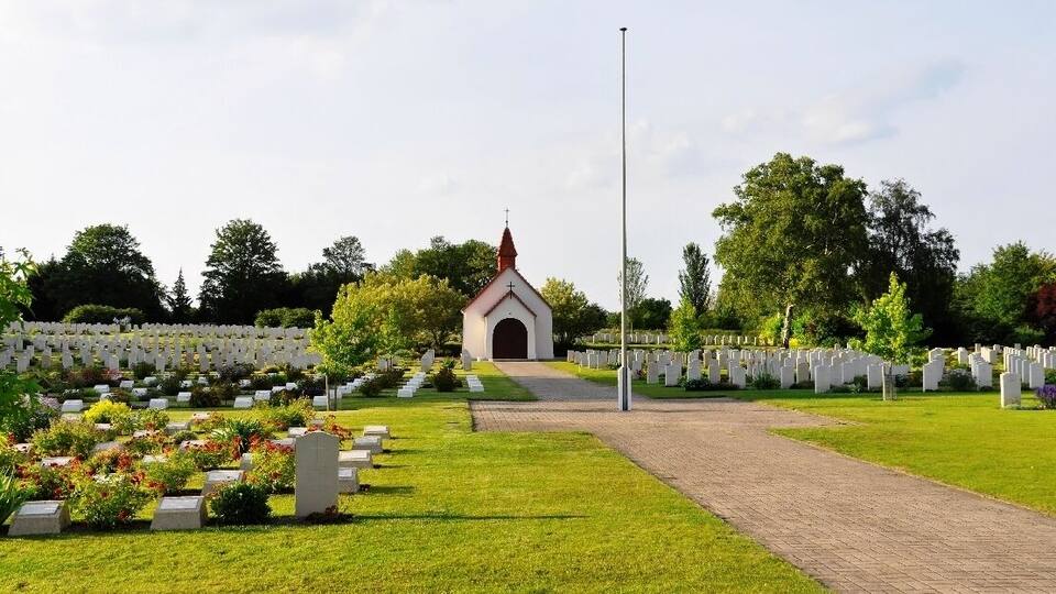 A cemetery with white headstones, a central building, and a clear sky.