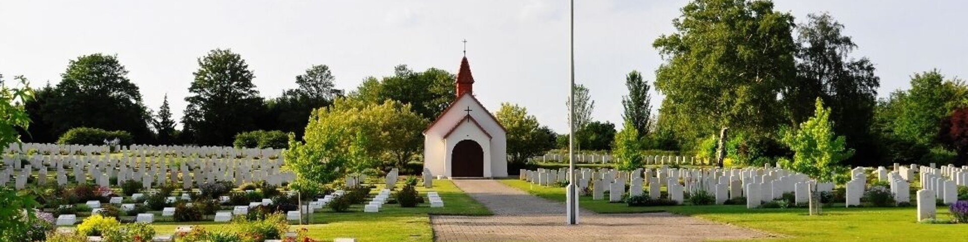 Un cementerio con lápidas blancas, un edificio central y un cielo despejado.