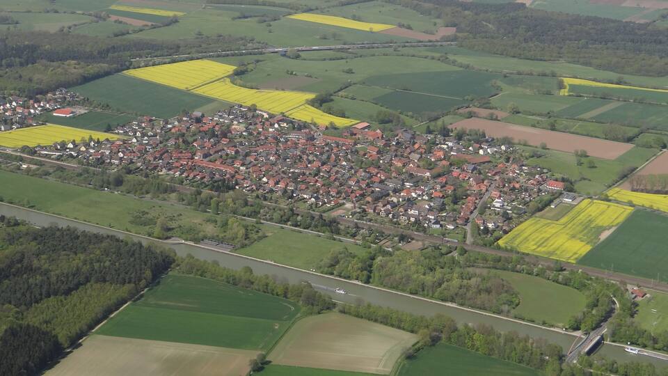 An aerial view of a rural town with fields, a river, and a bridge.