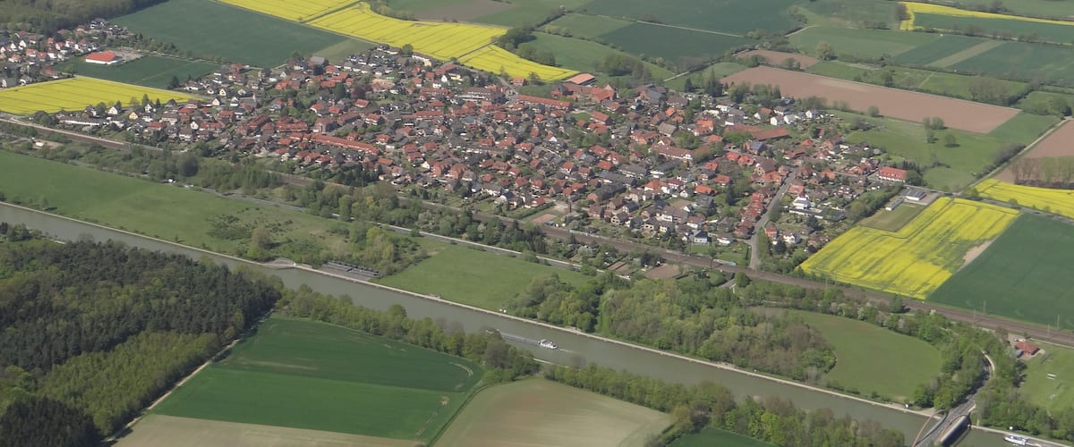 An aerial view of a rural town with fields, a river, and a bridge.