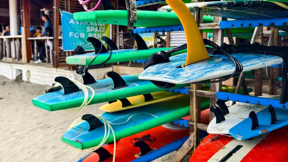 A collection of colorful surfboards stacked on a wooden rack on a sandy beach.