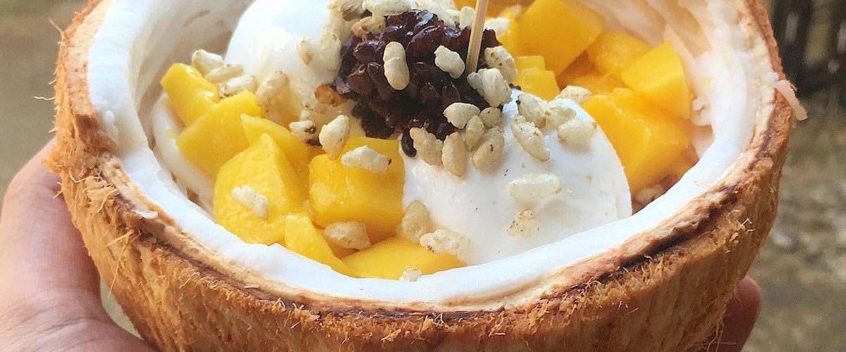 A coconut bowl with mango chunks, coconut ice cream, and nuts.