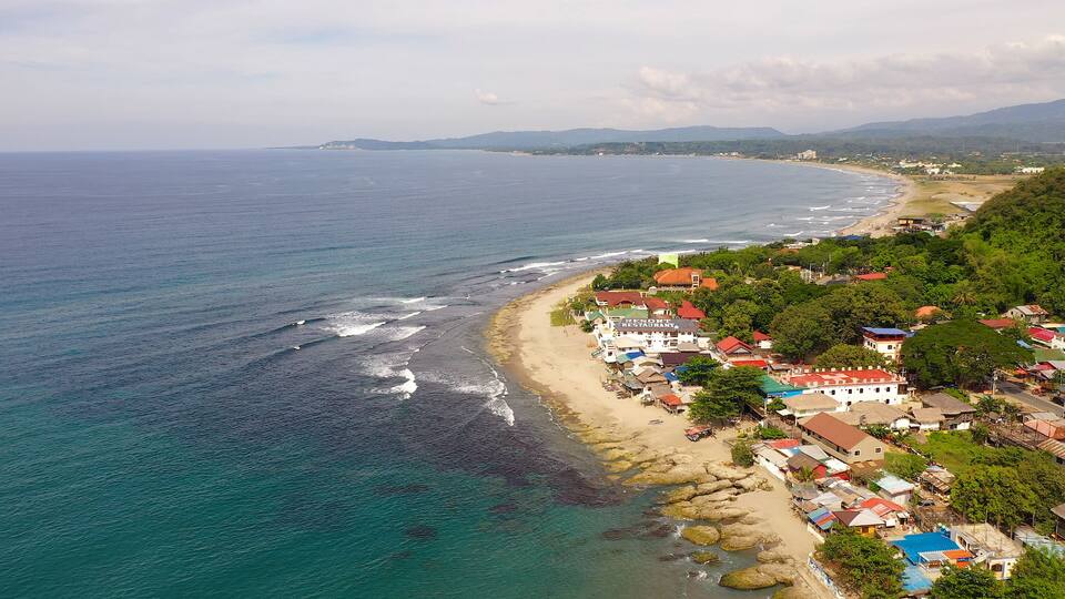 A coastal town with a beach, rocky shoreline, and buildings with red roofs.