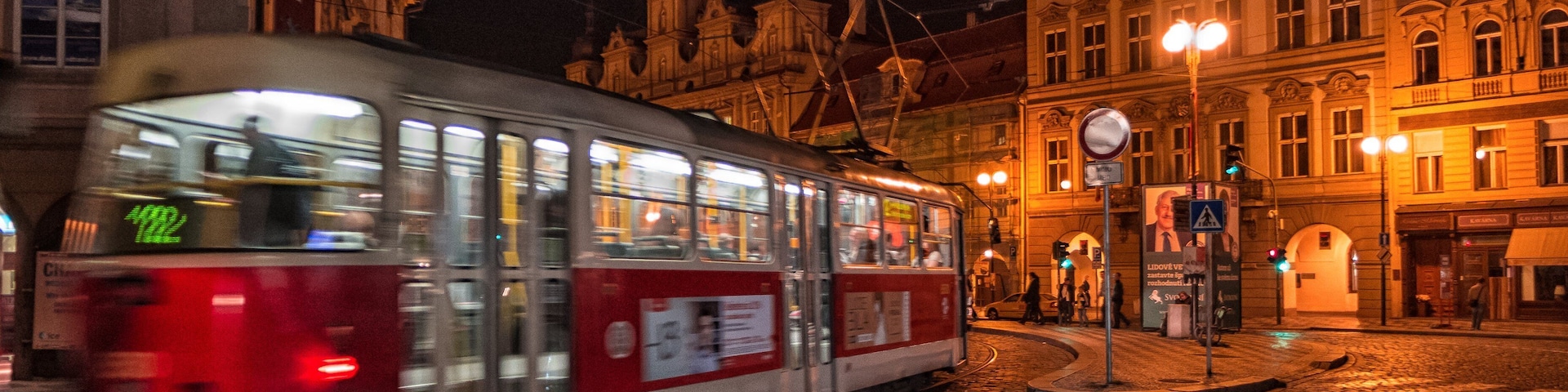 Un tranvía circulando por una calle empedrada de noche, con edificios históricos y farolas al fondo.