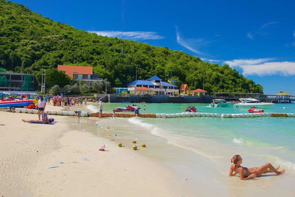 A beach with people sunbathing, a lifeguard tower, and boats in the water.
