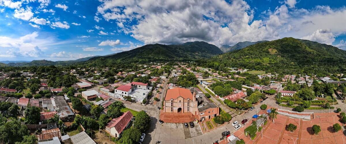 A town with a prominent church, surrounded by lush green hills and mountains.