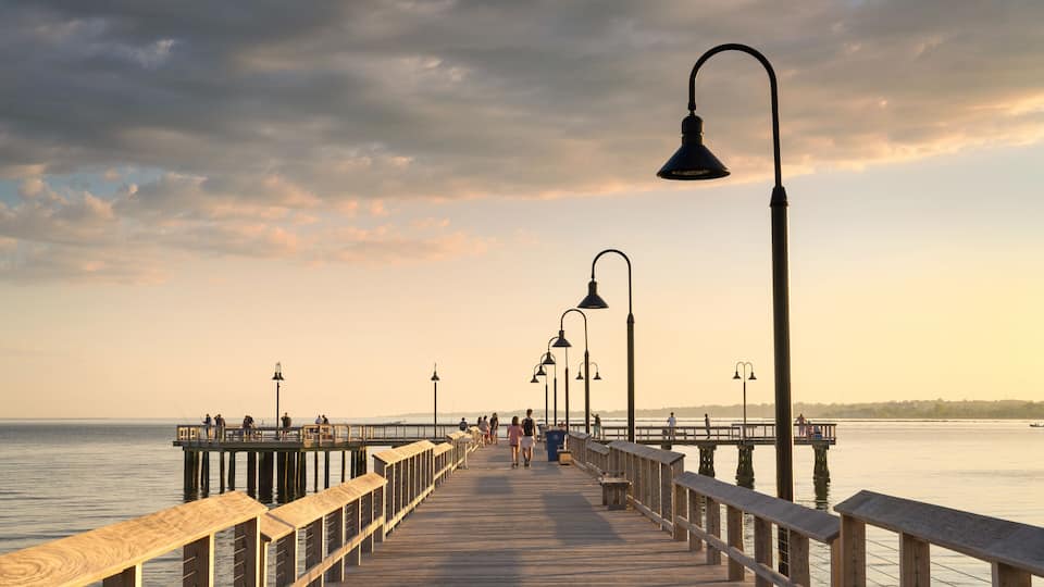 A wooden pier extending into calm waters, lined with street lamps and benches.