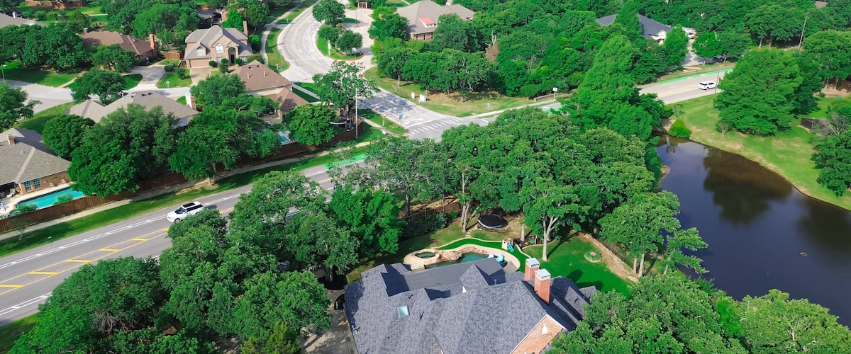 An aerial view of a residential area with houses, a winding road, a swimming pool, and a river.
