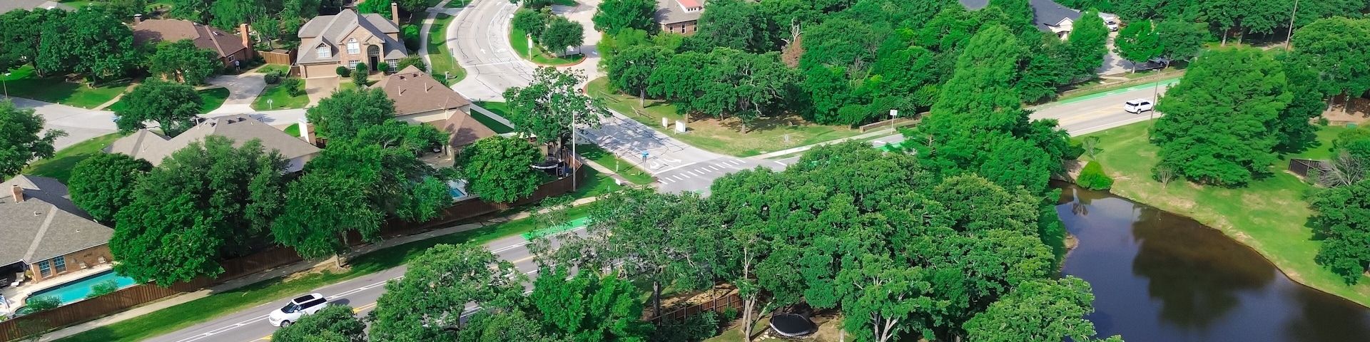 An aerial view of a residential area with houses, a winding road, a swimming pool, and a river.