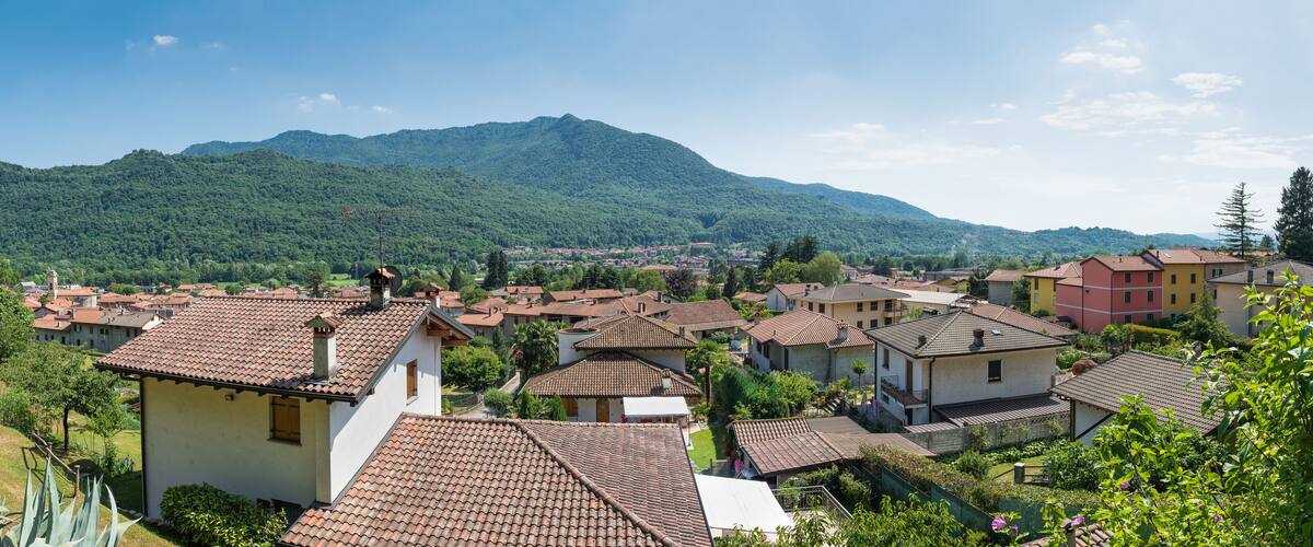 A town with red-tiled roofs, surrounded by lush green hills and a mountain in the background.