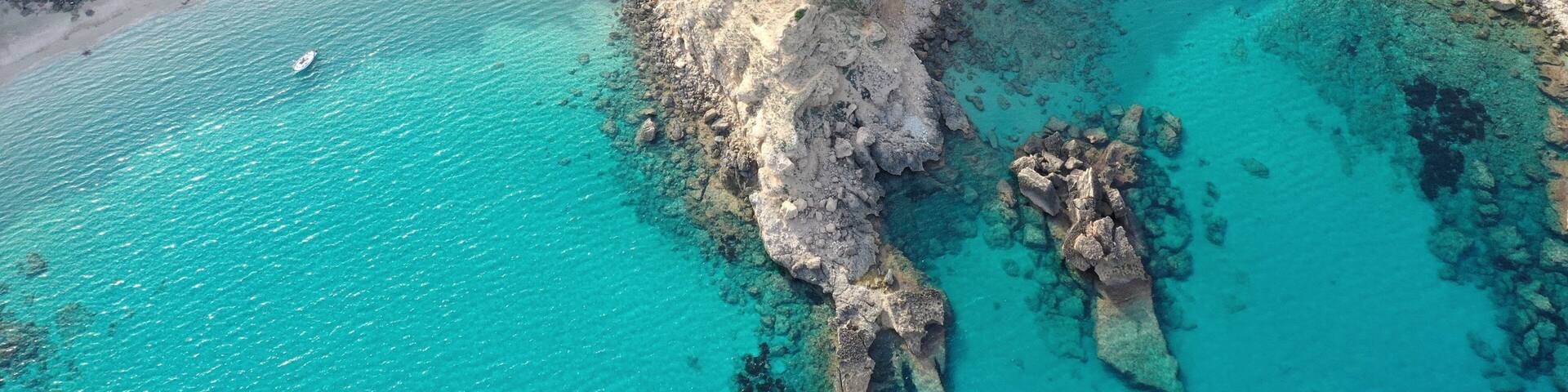 A coastal landscape with clear turquoise waters, rocky cliffs, and a small boat on the water.