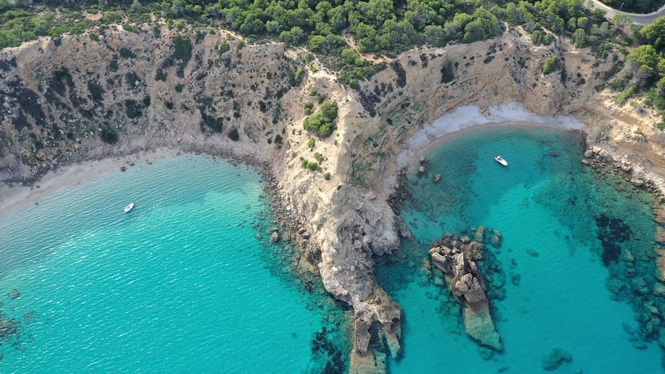 A coastal landscape with clear turquoise waters, rocky cliffs, and a small boat on the water.