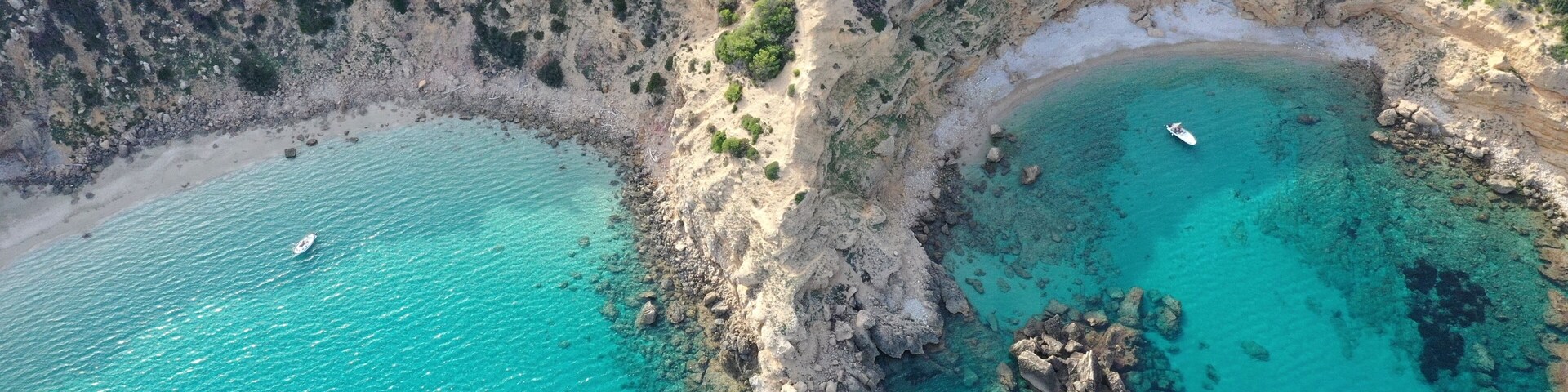 A coastal landscape with clear turquoise waters, rocky cliffs, and a small boat on the water.