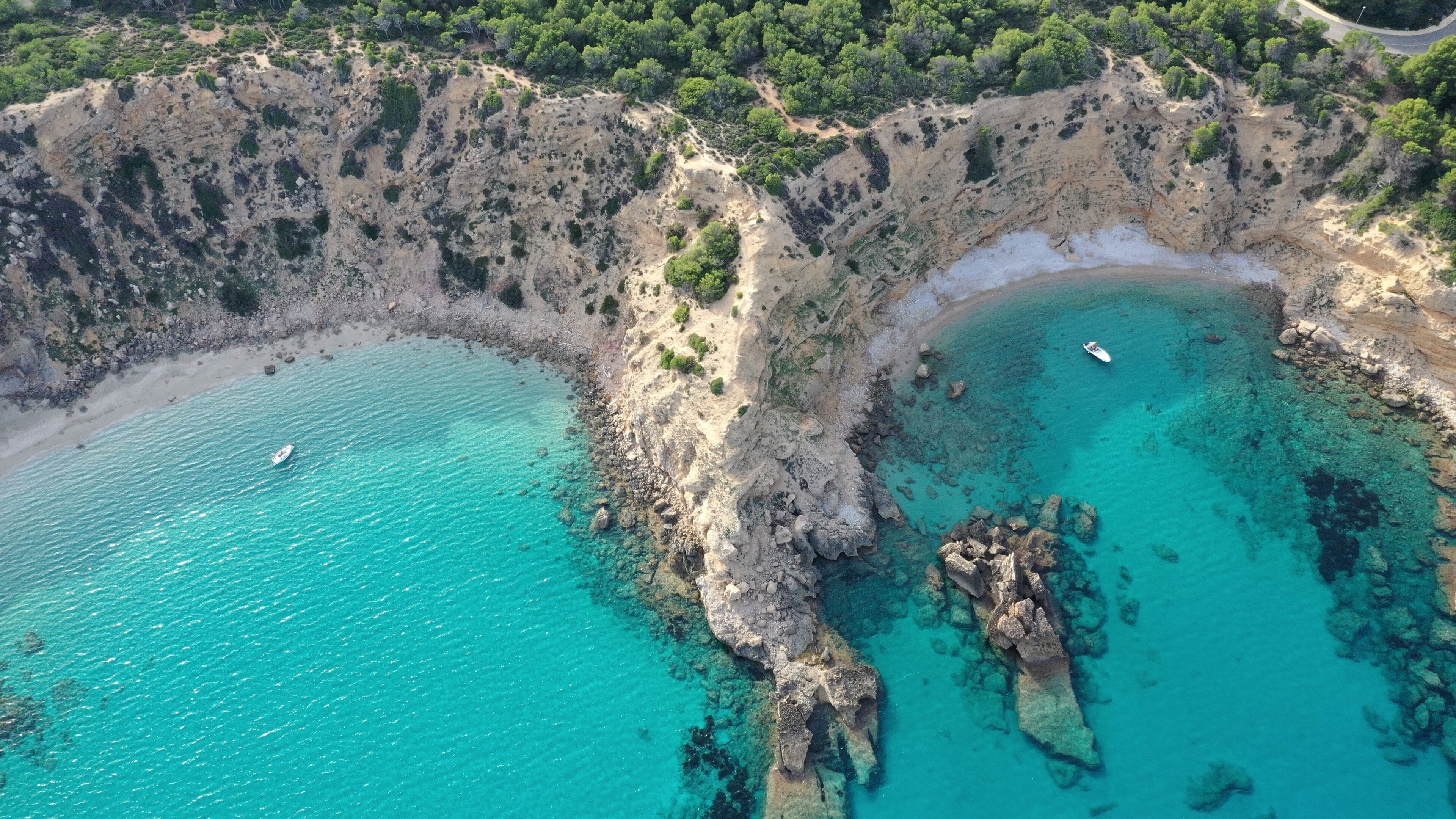 A coastal landscape with clear turquoise waters, rocky cliffs, and a small boat on the water.