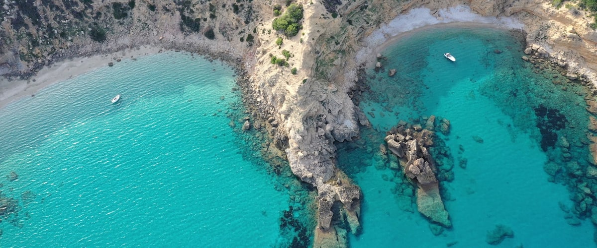 A coastal landscape with clear turquoise waters, rocky cliffs, and a small boat on the water.