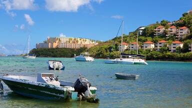 A coastal scene with several boats anchored near a building complex with red roofs.