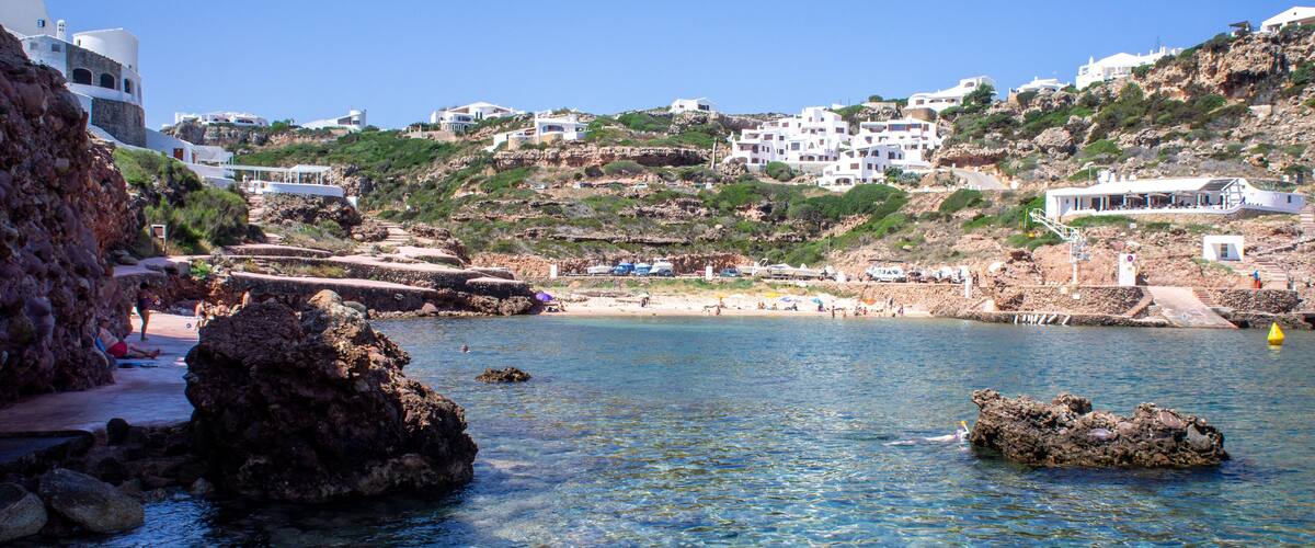 A coastal town with clear waters, rocky outcrops, and white buildings on a hillside.