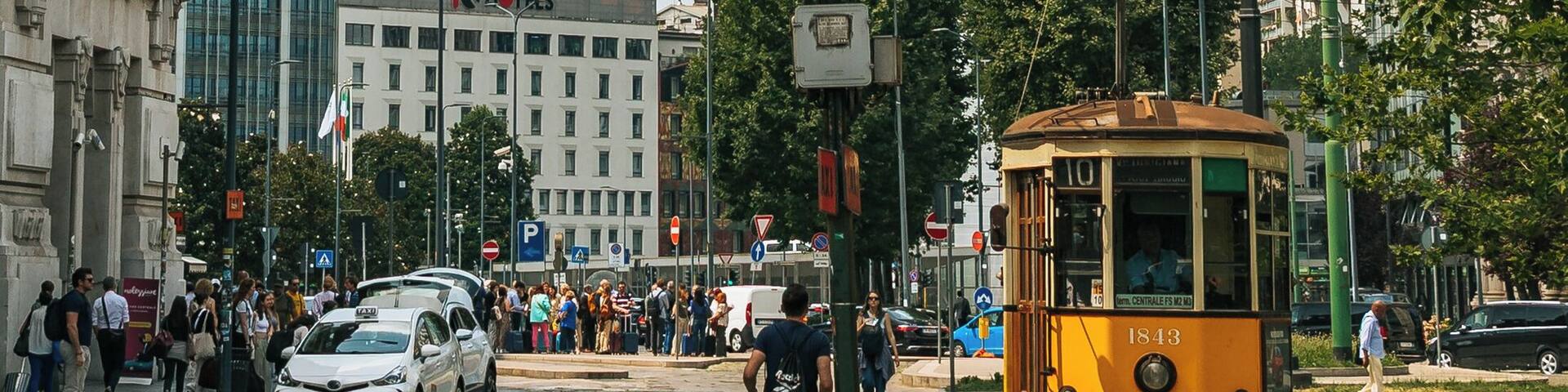 Un tranvía sobre rieles, un edificio alto y una calle concurrida con peatones y automóviles.