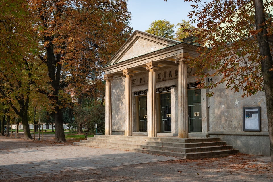 A classical building with columns and a pediment, surrounded by trees with autumn leaves.