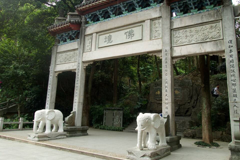 A traditional Chinese gate with inscriptions, surrounded by lush greenery and stone elephants.