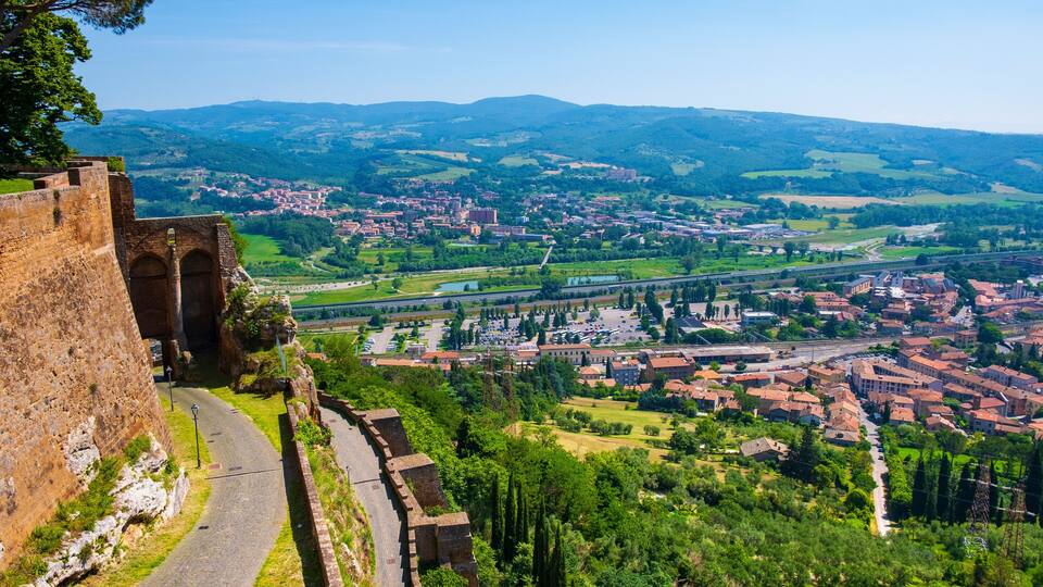 A historic stone wall with a paved path, overlooking a town with red-roofed buildings and green fields.